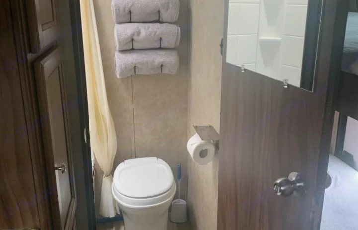 Compact RV rental bathroom features a toilet, shower curtain, stacked towels, and toilet paper, maximizing small space.. Coachmen Clipper 2018