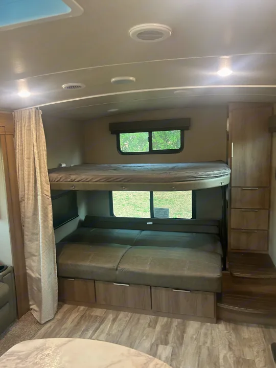 Inside this rv rental, bunk beds, a convertible lower sofa, and storage cabinetry create a functional space. Windows offer outdoor views.. Grand Design Imagine 2021