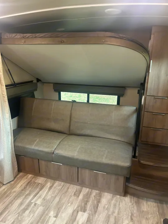 RV rental: a cozy gray sofa with under-seat storage, an overhead bunk bed, and wood-look flooring in this camper's interior.. Grand Design Imagine 2021