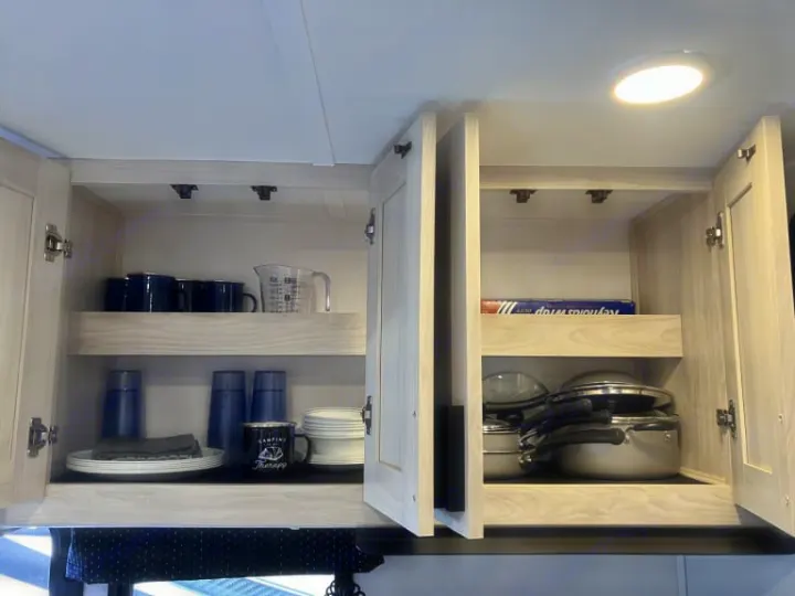 RV rental kitchen storage: neatly organized light wood cabinets filled with dinnerware, mugs, and cooking supplies.. Forest River Forester 2026