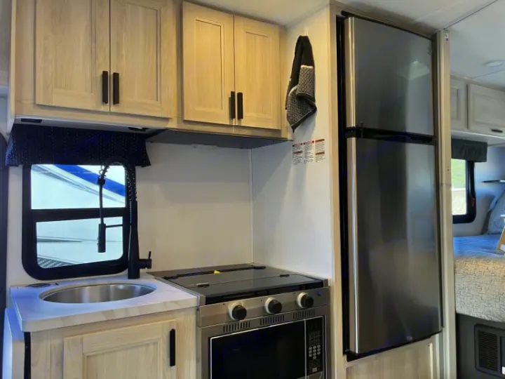 Modern rv rental kitchen featuring light wood cabinets, stainless steel fridge, sink, and stove with oven. Compact and functional.. Forest River Forester 2026