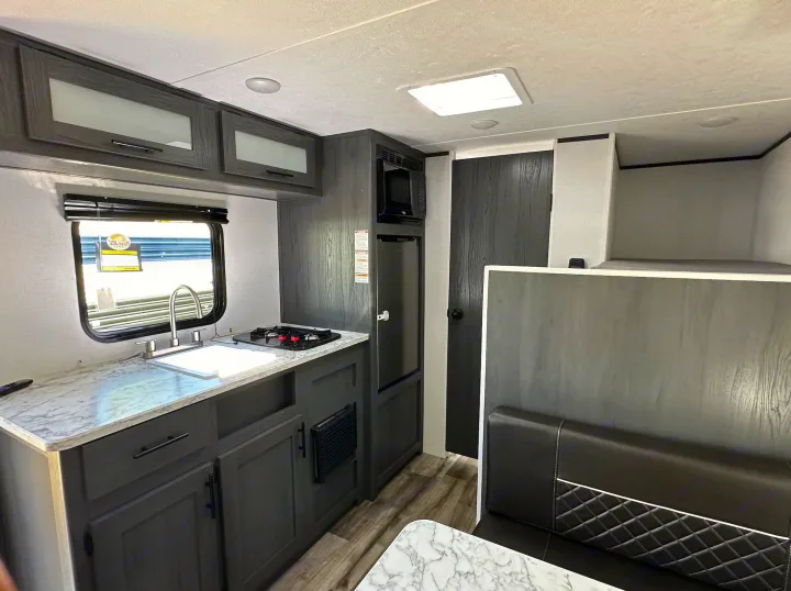 Modern RV rental interior featuring a compact kitchen, dining booth, and bunk beds. Stylish gray cabinets and marble counters.. Dutchmen Other 2024