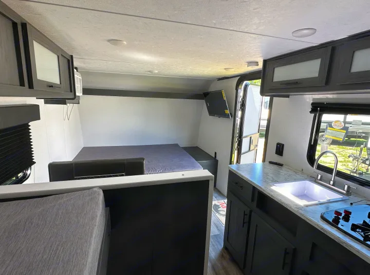 RV rental interior showing a compact living area with a bed, kitchen counter, sink, stovetop, and storage cabinets.. Dutchmen Other 2024