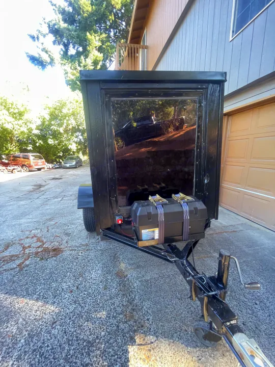 A black enclosed utility trailer, equipped with a battery box for power, suggesting RV rental possibilities. It's parked on a driveway.. Custom Squaredrop Trailer 2020