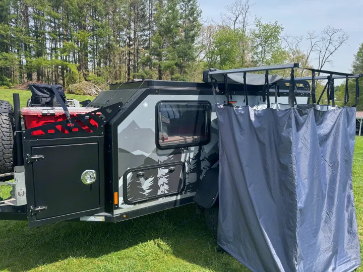 Compact off-road rv rental, gray with mountain graphics, features an attached outdoor privacy screen, ideal for camping.. Mission Overland Summit 2024