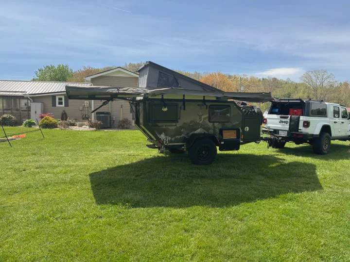 Off-road RV rental: a green overland trailer with an awning extended, hitched to a white Jeep Gladiator, ready for adventure.. Mission Overland Summit 2024