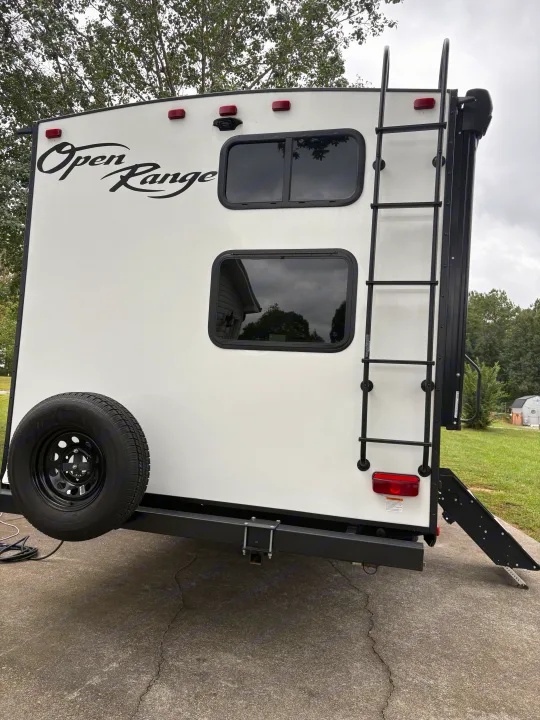 The rear of a white Open Range travel trailer RV rental, equipped with a spare tire, ladder, and two tinted windows.. Highland Ridge RV Range Lite 2021