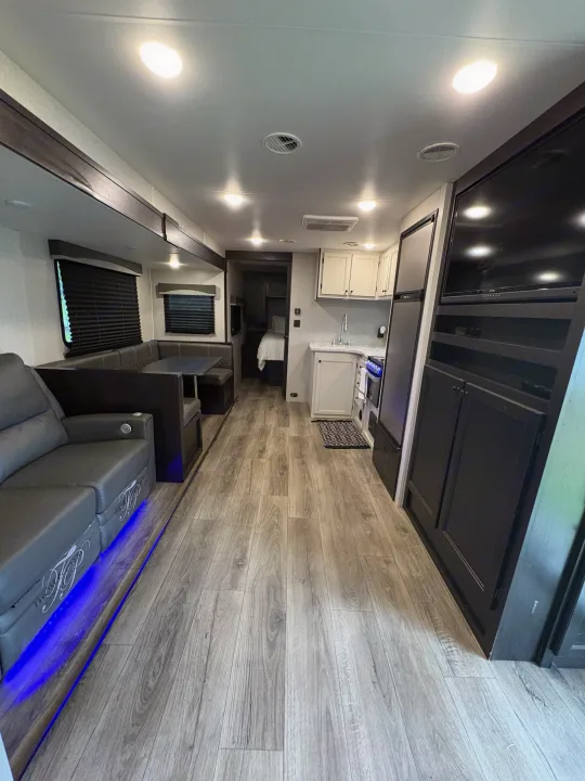 Spacious RV rental interior featuring a modern kitchen, comfortable living/dining areas, and a cozy bedroom. Blue LED lighting adds ambiance.. Highland Ridge RV Range Lite 2021