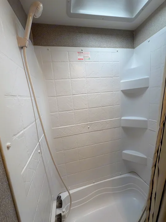 Inside an RV rental, a clean shower stall features a handheld showerhead, built-in shelves, and a compact tub.. Highland Ridge RV Range Lite 2021