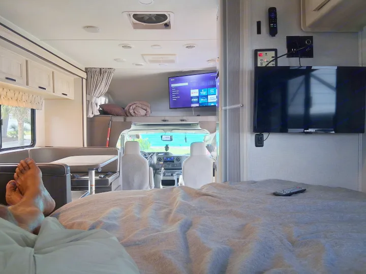 Cozy RV rental interior: feet up on bed, watching streaming TV (Roku, Netflix) while parked, with the dinette and cab visible.. Forest River SLE 2021