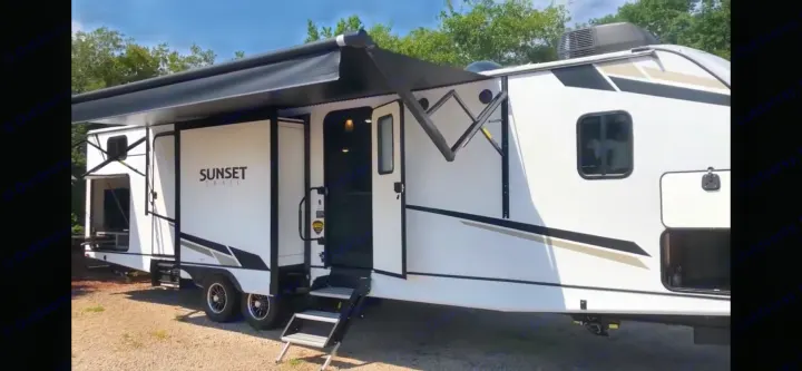 This white Sunset Trail RV rental, featuring an extended awning, open door with steps, and outdoor kitchen, is ready for adventure.. Crossroads RV Sunset Trail Super Lite 2023