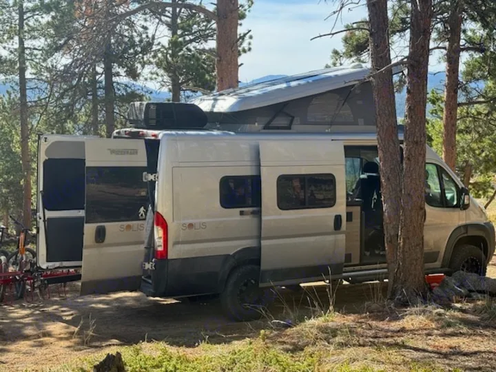 RV rental adventure: Two Winnebago Solis campervans, one with a pop-top, parked among trees with bikes.. Winnebago Solis 2022