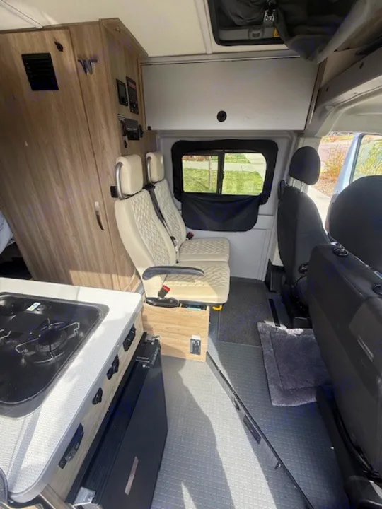 Spacious rv rental interior: A modern camper van features a kitchenette, two light quilted passenger seats, and overhead storage.. Winnebago Solis 2022
