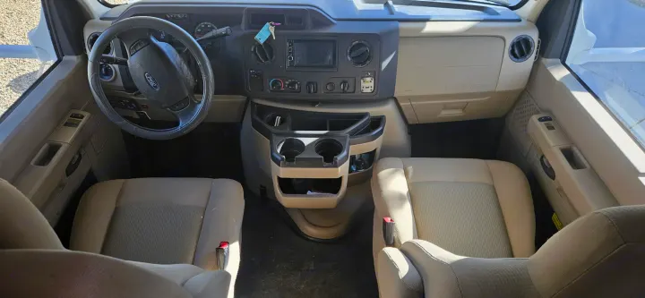 Spacious RV rental front cabin showcasing a Ford steering wheel, dashboard, cup holders, and light-colored driver/passenger seats.. Thor Freedom Elite 2017