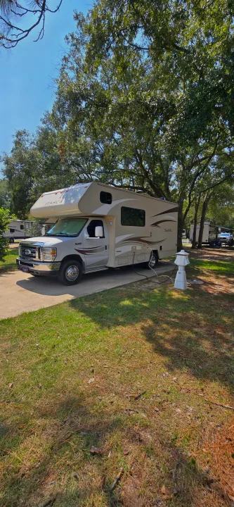 An Itasca Spirit Class C rv rental at a shady campsite, connected to utility hookups. Other RVs nearby.. Winnebago Minnie Winnie 2019