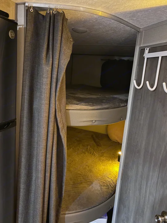 Cozy rv rental bunk beds with a privacy curtain and soft lighting, ideal for family travel accommodations.. Coachmen 184BH 2025