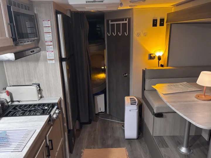 A well-equipped RV rental interior with a kitchen (microwave, stovetop), cozy dinette, and compact living space.. Coachmen 184BH 2025