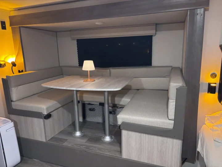 Cozy RV rental dinette featuring U-shaped light grey seating, a marble-look table, soft lighting, and under-seat storage bins.. Coachmen 184BH 2025