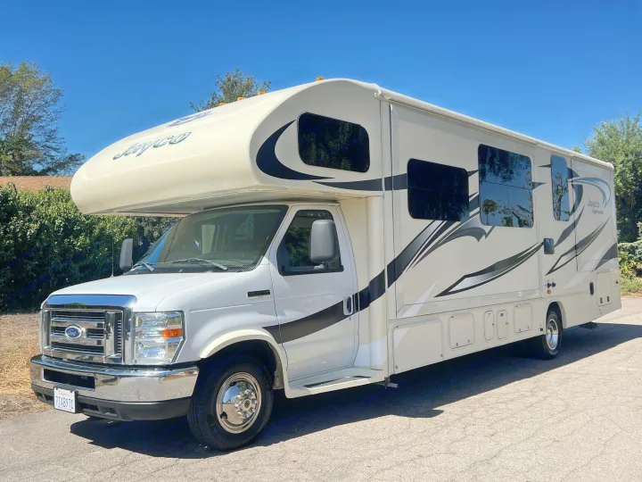 This white Jayco Greyhawk Class C **rv rental**, with black graphics, is parked under a blue sky, ready for adventure.. Jayco Greyhawk 2016