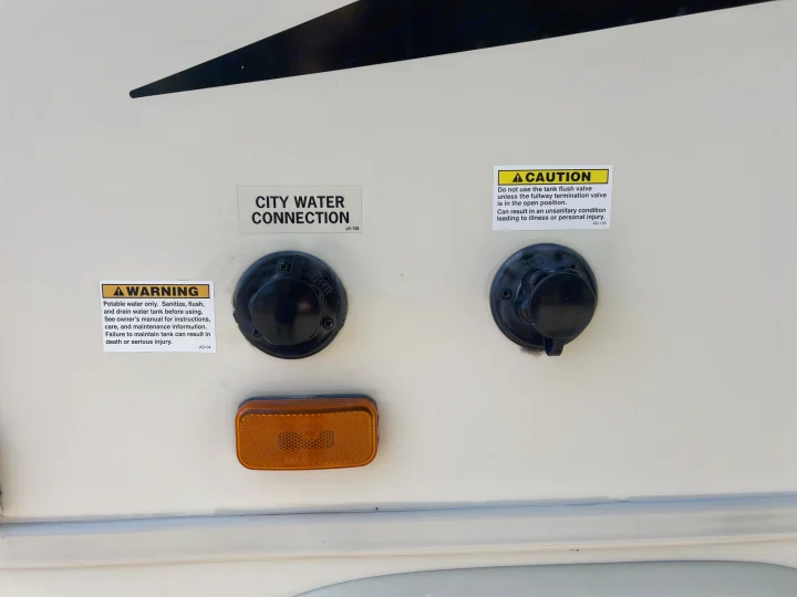 RV rental exterior with city water connection, tank flush, and essential warning labels for potable water and tank maintenance.. Jayco Greyhawk 2016