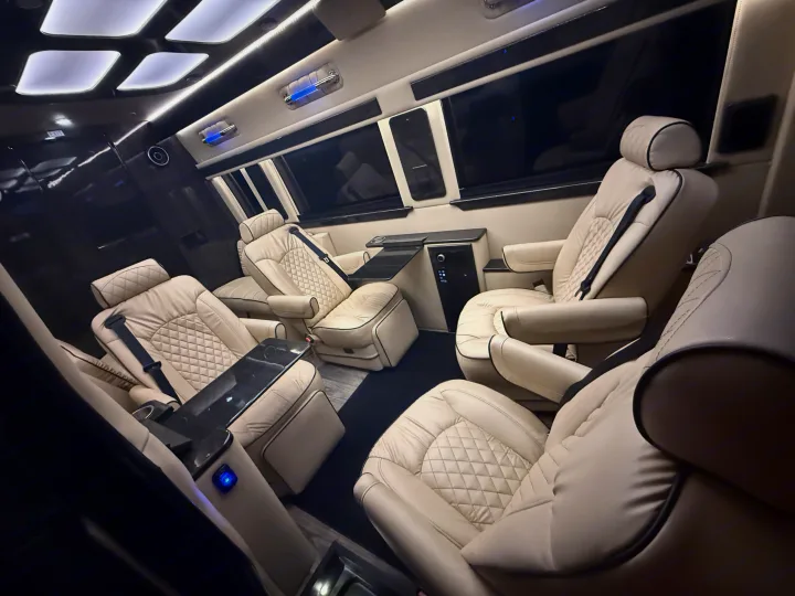 Luxurious private RV rental interior featuring cream quilted leather captain's chairs, tables, and ambient lighting for ultimate comfort.. Ultimate Toys Ultimate Coach 2023