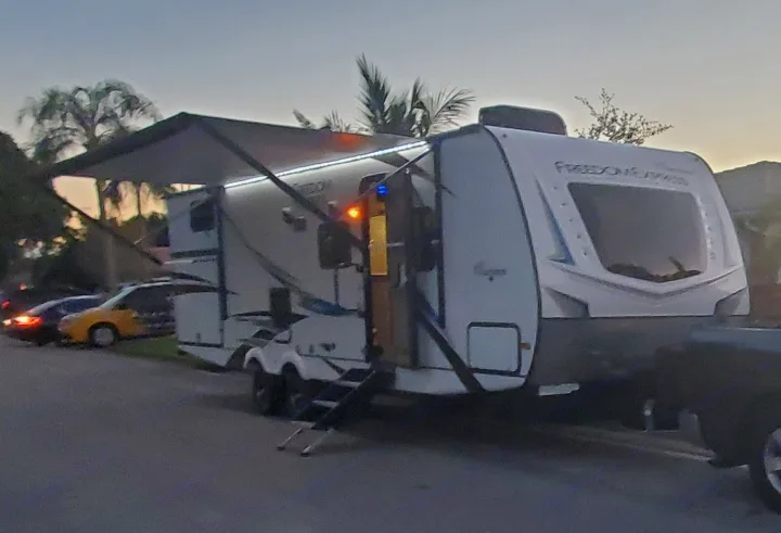 This RV rental travel trailer is parked with an extended awning and lights at dusk, hooked to a truck, ready for camping.. Coachmen 292BHDS 2021
