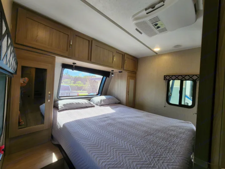 Bright and inviting RV rental bedroom featuring a large bed, overhead cabinets, front window view, and mirrored closet for comfort.. Coachmen 292BHDS 2021
