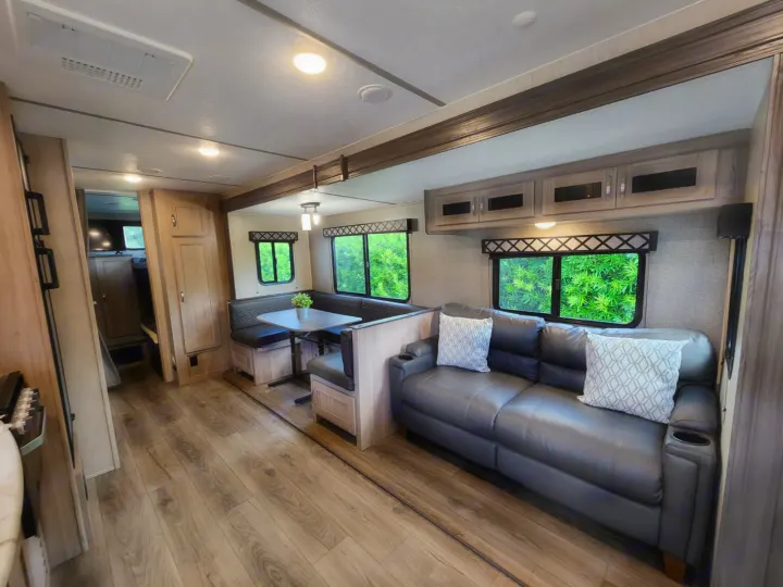 This modern RV rental living area features a cozy sofa, dinette with benches, and bright windows for comfortable travel.. Coachmen 292BHDS 2021