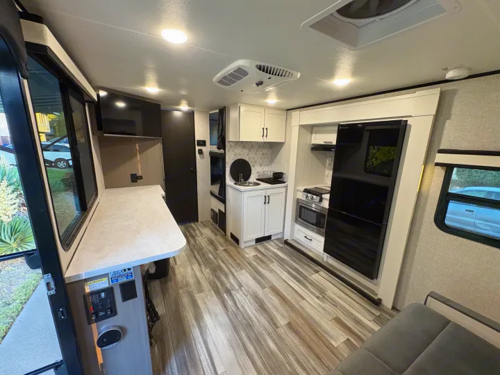 Modern rv rental interior: kitchen with microwave/fridge, dining counter, comfy seating, bunk beds, and wood-look flooring.. Jayco Jay Feather 18MBH 2025
