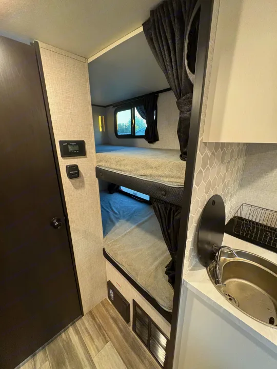 This RV rental interior features cozy bunk beds, a compact sink area with hexagon backsplash, and wall controls. Ideal for adventure.. Jayco Jay Feather 18MBH 2025