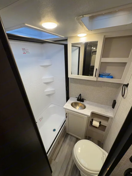 Compact RV rental bathroom with a white shower, toilet, modern vanity, sink, mirror, and skylights. Perfect for adventures.. Jayco Jay Feather 18MBH 2025