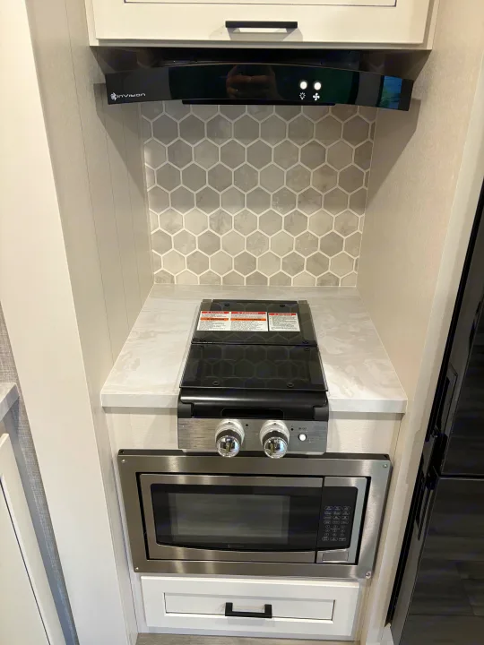 RV rental kitchen features an InVision range hood, stovetop, and microwave, complemented by a stylish hex tile backsplash.. Jayco Jay Feather 18MBH 2025
