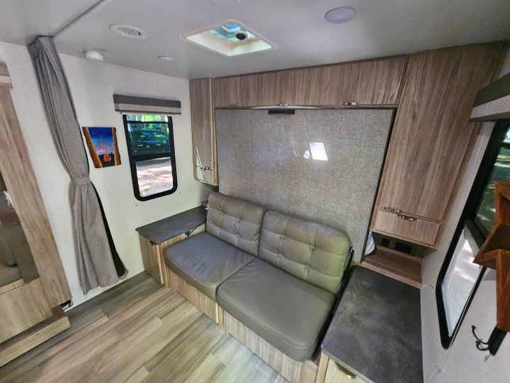 Inside this RV rental: A compact yet comfortable camper living area featuring a sofa, wall bed, and storage cabinets.. Winnebago Minnie 2201MB 2022