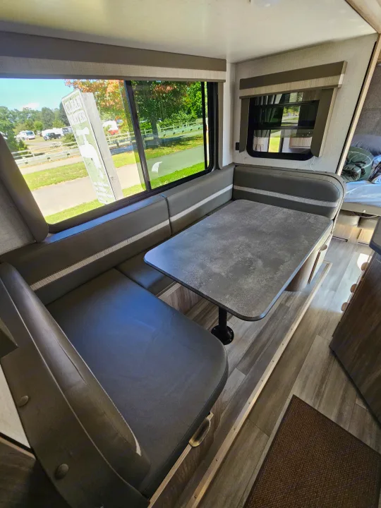 Enjoy your RV rental! This inviting dinette area offers comfortable booth seating and a window view of a sunny campground.. Winnebago Minnie 2201MB 2022
