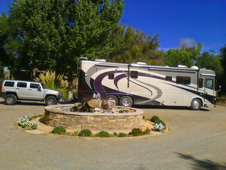 An RV rental and a Hummer are parked next to a decorative rock fountain under a clear blue sky, surrounded by green trees.. Country Coach Allure 470 2005