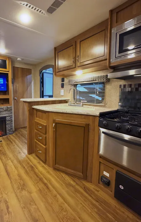 RV rental interior: fully equipped kitchen with wood cabinets, sink, stove, microwave, and laminate flooring. Offers a cozy, functional space.. Coachmen Catalina 2017