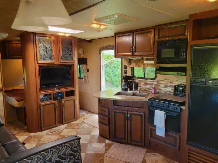 Spacious RV rental interior with a full kitchen, living area with TV, and a glimpse of a cozy bedroom.. Crossroads RV Zinger 2015