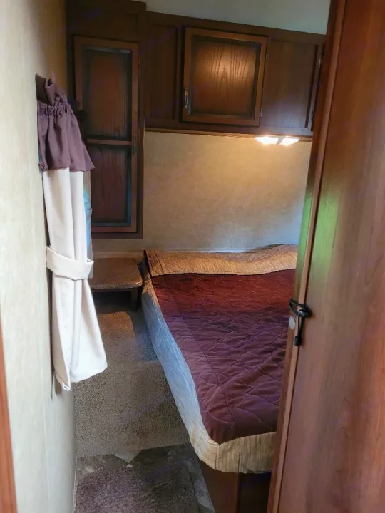 Cozy RV rental bedroom with a comfortable bed, dark wood cabinets, nightstand, and overhead lighting for your travels.. Crossroads RV Zinger 2015