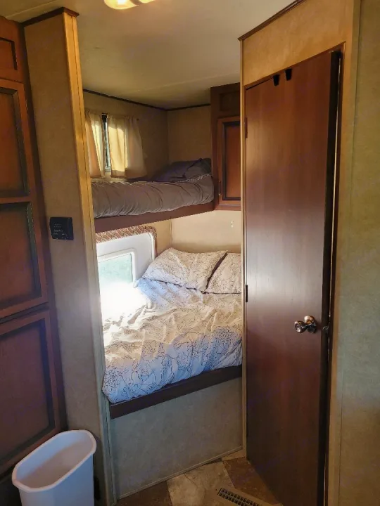 Cozy RV rental bunk beds, perfect for family adventures. Features two bunks, a window, and a nearby door.. Crossroads RV Zinger 2015