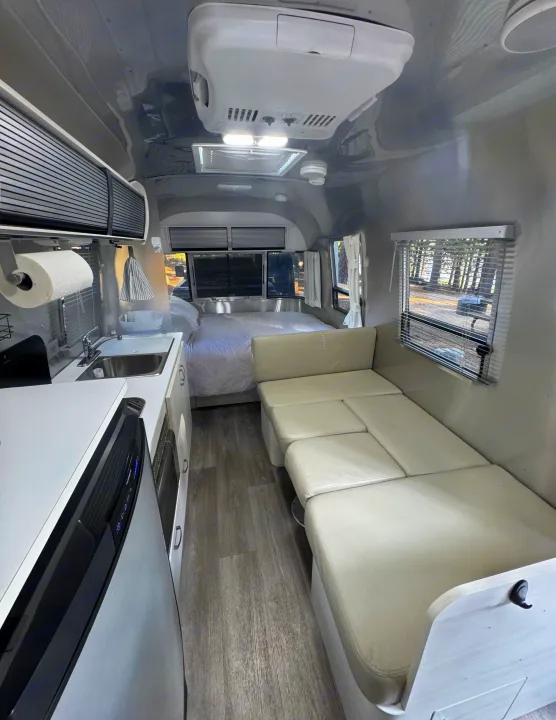 Bright and clean rv rental interior featuring a compact kitchen, cozy bed, and convertible lounge seating in a modern camper.. Airstream Sport 2018