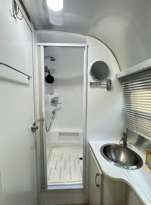 Inside a compact rv rental bathroom: a sleek shower, stainless steel sink, extendable mirror, and vanity unit.. Airstream Sport 2018