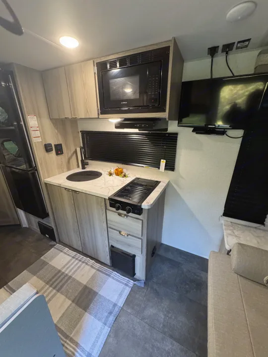 This RV rental galley features a microwave, sink, two-burner stove, refrigerator, TV, and light wood cabinetry.. Forest River Salem 2024
