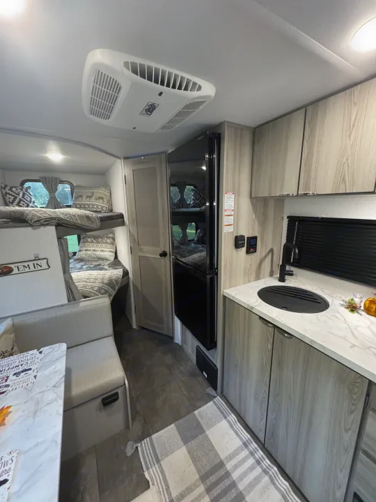 Cozy rv rental interior showing bunk beds, a dinette, and a kitchen with light wood cabinets and a modern black sink.. Forest River Salem 2024