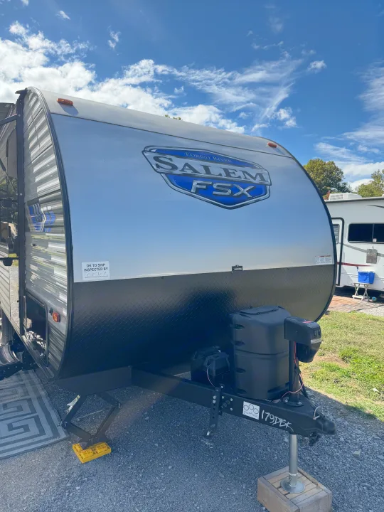 A silver and black Forest River Salem FSX travel trailer, ideal for an RV rental, parked on gravel under blue skies.. Forest River Salem 2024