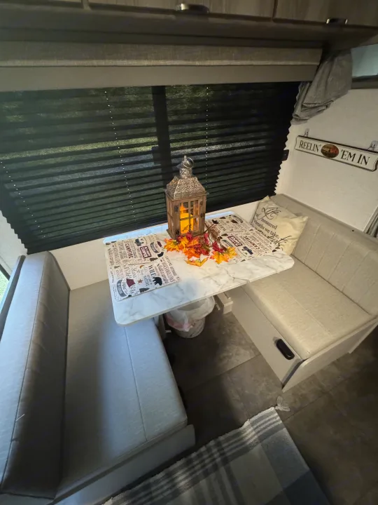 An RV rental's cozy dinette with autumn decor, a lit lantern, and benches provides a warm space for travelers.. Forest River Salem 2024
