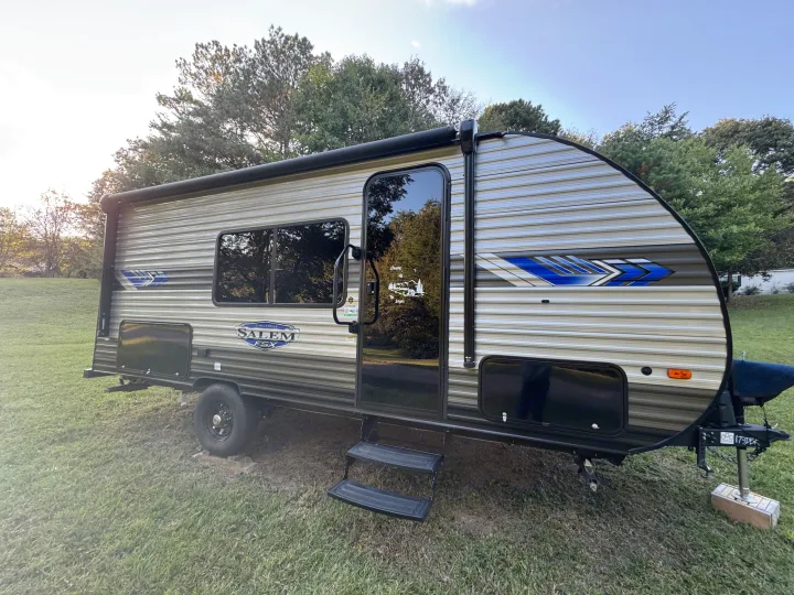 This Forest River Salem FSX RV rental, a small travel trailer with awning and steps, is parked on grass for outdoor adventures.. Forest River Salem 2024