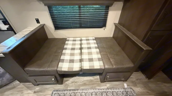 Inside an RV rental: a comfortable dinette with dark benches, plaid seat cushions, and convenient under-seat storage.. Grand Design Transcend Xplor 2022