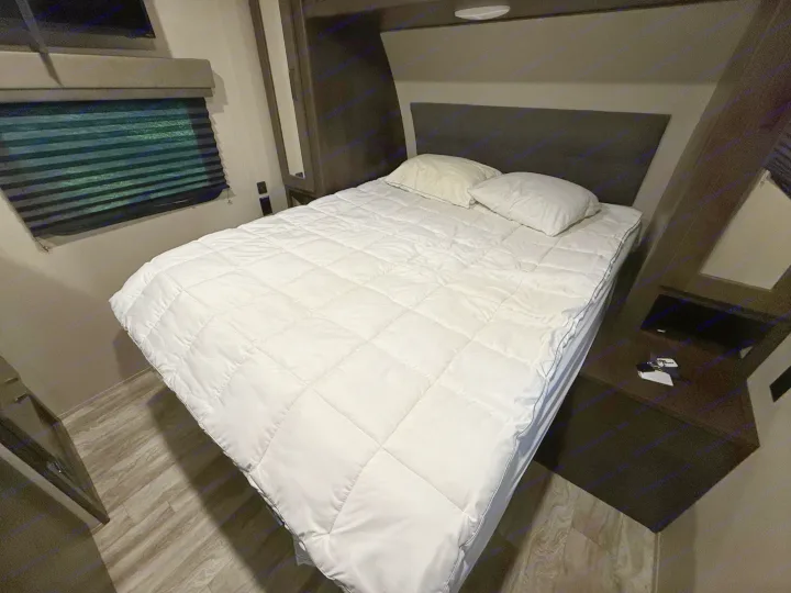 Cozy RV rental bedroom featuring a neatly made bed with a white comforter, pillows, and window blinds.. Grand Design Transcend Xplor 2022