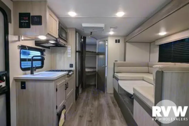 This modern RV rental features a full kitchen with a sink, an L-shaped dinette, and bunk beds visible through an open door.. Coachmen 184BH 2025
