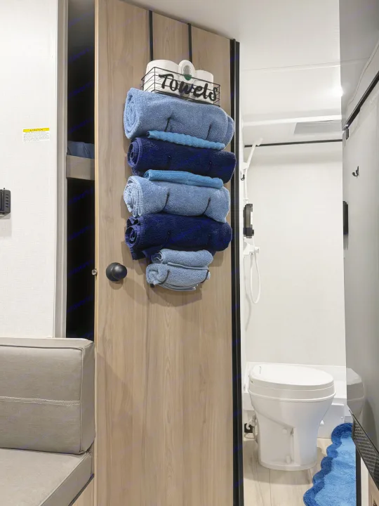 Organized rv rental interior featuring space-saving towel storage on the door, revealing a compact bathroom with toilet and shower.. Coleman 23B Keystone 2025